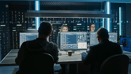 Quatre personnes surveillent des écrans d’ordinateur dans une salle serveur sombre éclairée en bleu.