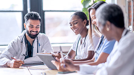 Un groupe de quatre jeunes médecins est assis à une table de réunion et discute du succès d'un traitement avec un dossier médical numérique sur une tablette.