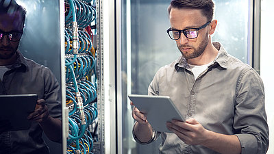 Un jeune informaticien à lunettes vérifie les valeurs de sécurité sur une tablette dans la salle des serveurs