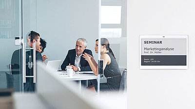 Un groupe d'employés de bureau discute avec animation dans une salle de conférence équipée d'un panneau de porte électronique.