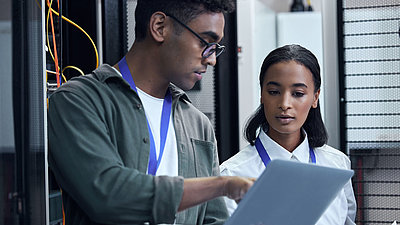 Un homme et une femme administrateurs informatiques se consultent dans la salle des serveurs sur un ordinateur portable pour une meilleure gestion du réseau