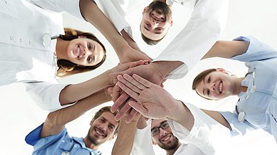 Équipe médicale empile les mains en souriant, symbole de collaboration et d’esprit d’équipe dans la santé.