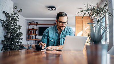 Un homme travaille sur un ordinateur portable dans son bureau à domicile et prend des notes sur un bout de papier