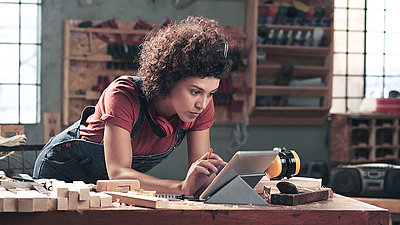 Une femme se tient dans un atelier et utilise une tablette.