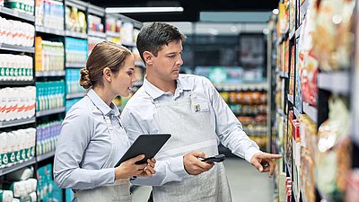 Une employée de supermarché équipée d'une tablette vérifie les marchandises en rayon avec son collègue équipé d'un scanner portatif