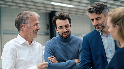 Quatre professionnels en discussion, souriants et concentrés dans un environnement technique moderne.