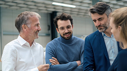 Quatre professionnels en discussion, souriants et concentrés dans un environnement technique moderne.