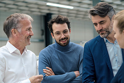 Quatre professionnels en discussion, souriants et concentrés dans un environnement technique moderne.