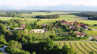 Vue aérienne d'un paysage verdoyant avec des fermes, des champs et des montagnes en arrière-plan par une journée ensoleillée.