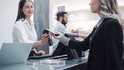 Une cliente blonde en blazer noir paie sans contact avec son smartphone à la caisse d'un magasin moderne.