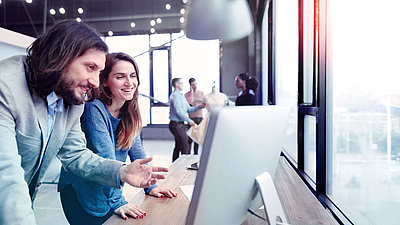 Femme et homme riant devant l'écran d'un PC dans un bureau moderne