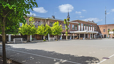 Photo de la grande cour verte et du bâtiment de l'école Sint Jozef Klein Seminarie avec un joli bâtiment en briques en arrière-plan, y compris un panier de basket, des bancs couverts, etc.