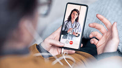 homme tenant un téléphone avec des écouteurs ; vous regardez l'écran d'en haut. Appel vidéo avec un médecin