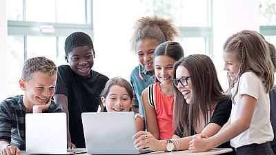 Une enseignante de l'école primaire montre avec enthousiasme quelque chose à ses élèves sur un ordinateur portable