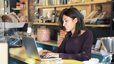 Une dame travaille avec son ordinateur portable au comptoir d'un bar dans un café