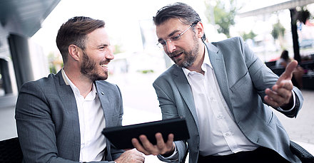 Deux hommes discutent en regardant une tablette